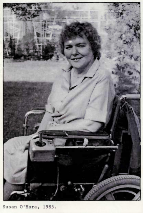 ID: grayscale photo of Susan O'Hara smiling in a short sleeved collared dress sitting in a wheelchair facing perpendicular from the camera