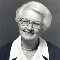  grayscale photo of Betty Connors, in thick frame glasses and a white collared blouse and gray sweater, smiling into the camera