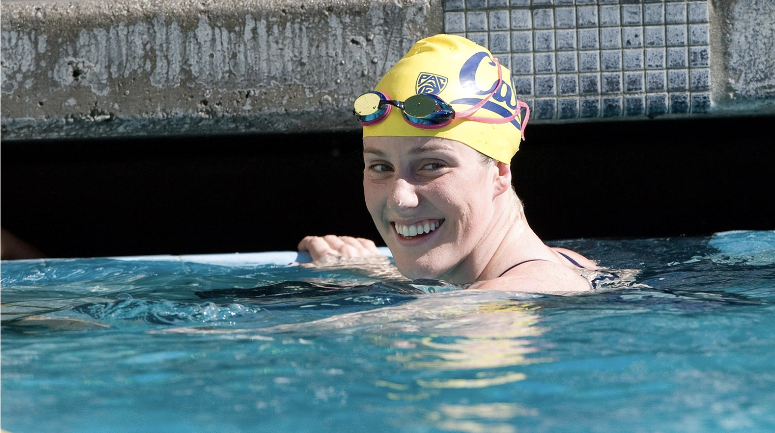 Woman smiling in yellow swim cap at end of pool lap lane