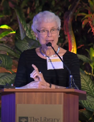  Dorothy Gregor in shiny necklace and black dress with name tag, mid-speech accepting an award at a podium