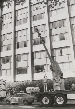  grayscale photo of a man directing crane lifting an iron lung into one of the rooms of the unit 2 residence hall