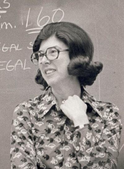  grayscale photo of Kay Young in flipped out haircut, abstract patterned blouse, and glasses staring off into the distance 