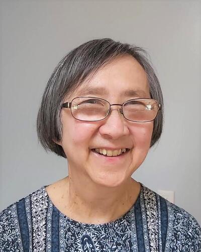  image of Sau-Ling Wong smiling with short hair, glasses and dark blue top with white patterns against gray background 