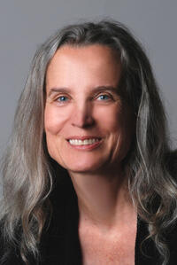  headshot of Susan Schweik smiling in black top and medium-length hair against a gray background